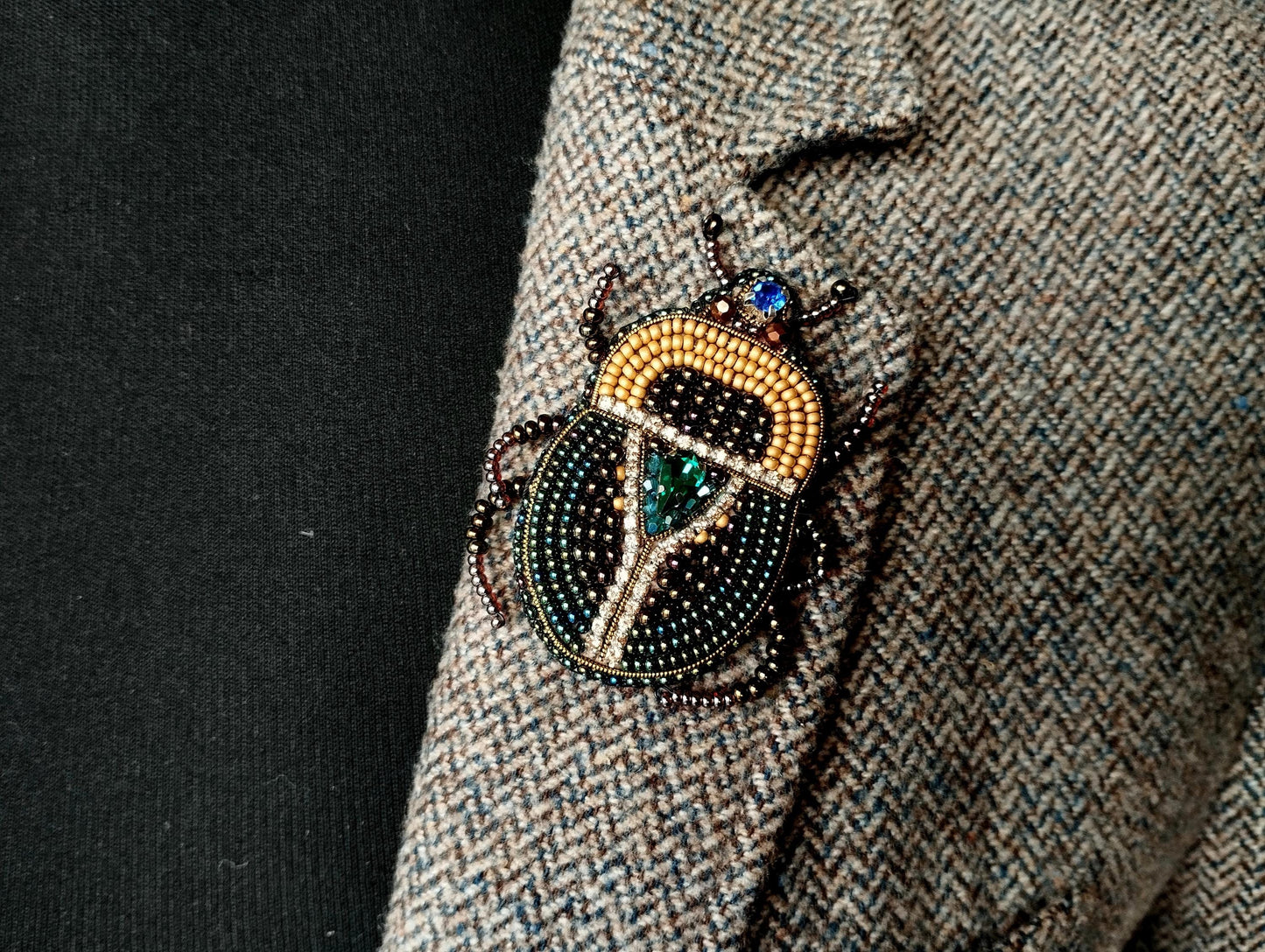 A close-up of a decorative insect brooch on a tweed jacket lapel.