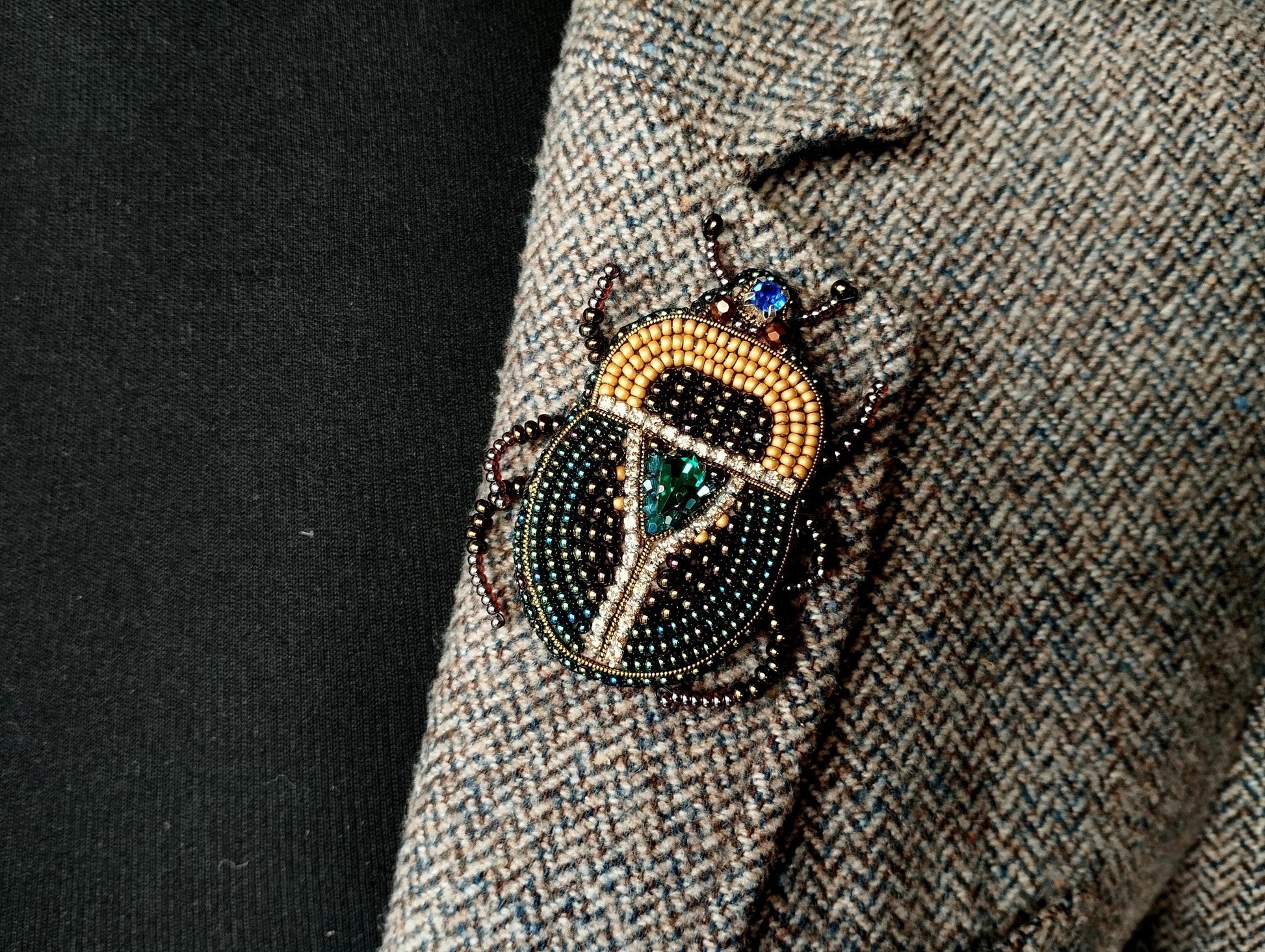 A close-up of a decorative insect brooch on a tweed jacket lapel.