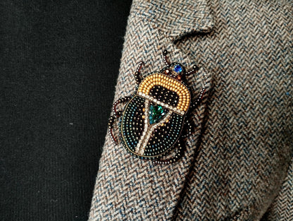 A close-up of a decorative insect brooch on a tweed jacket lapel.