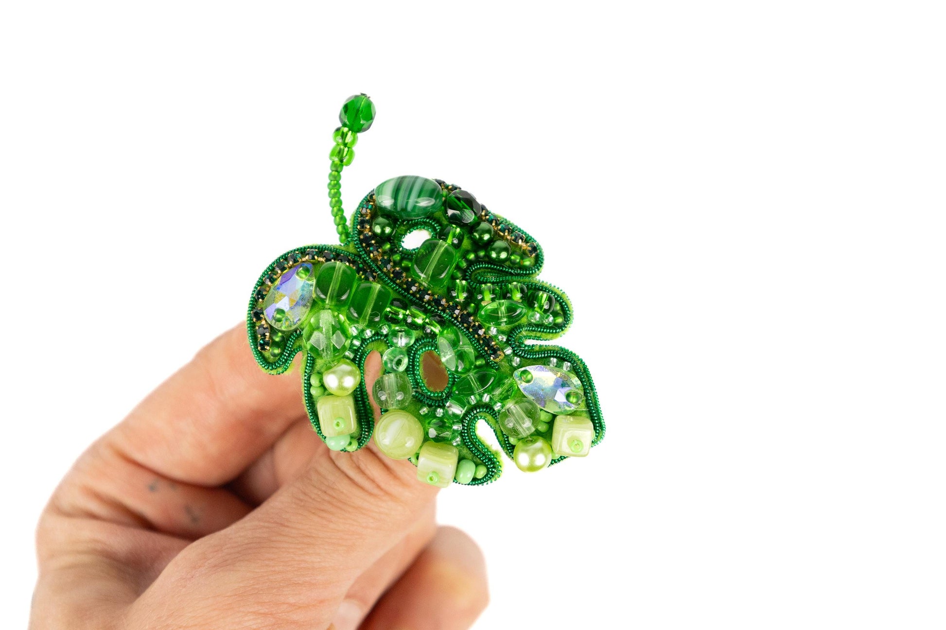 a hand holding a green beaded brooch