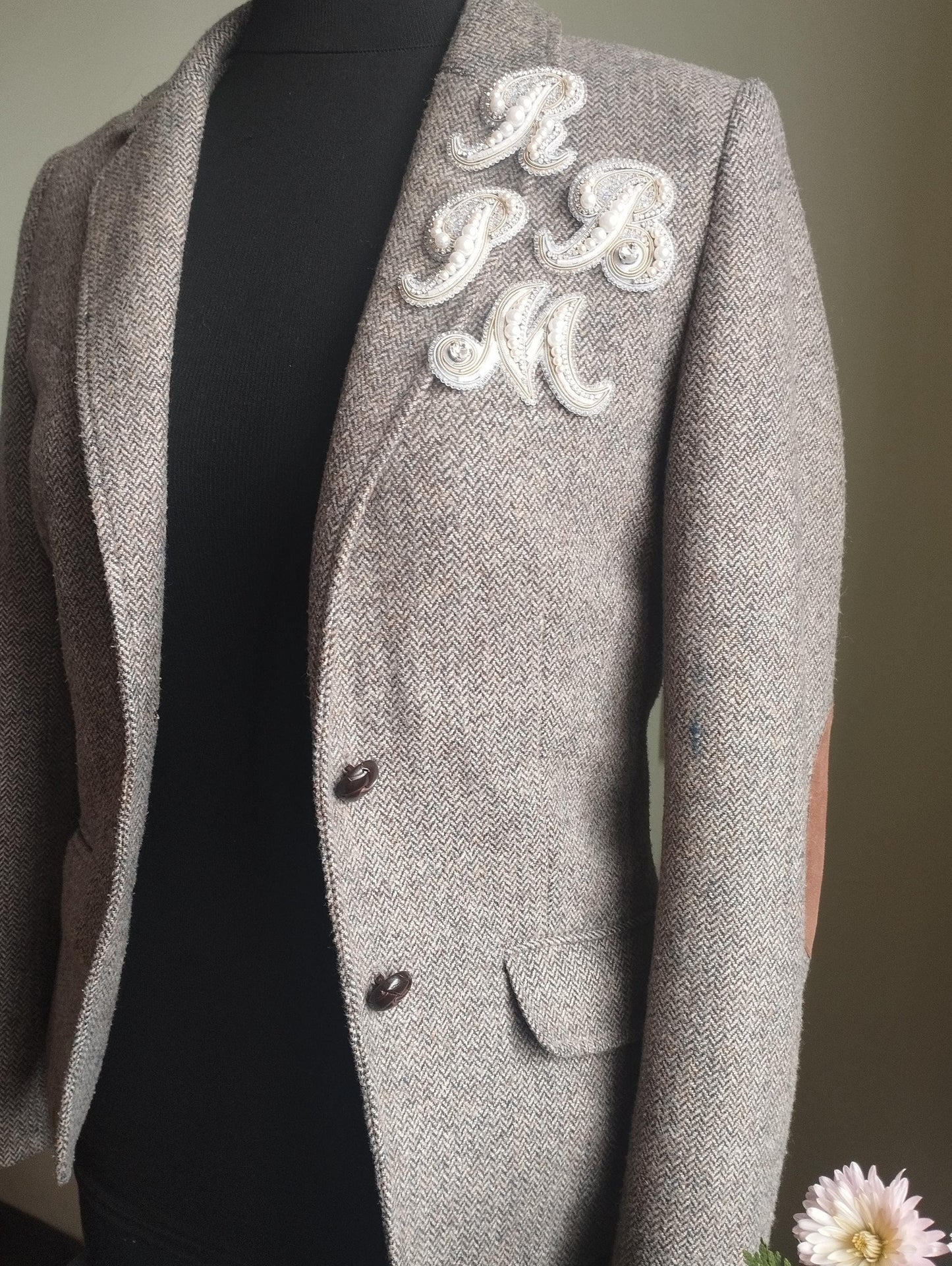 a gray tweed jacket with a monogrammed monogram on the left side of the chest.