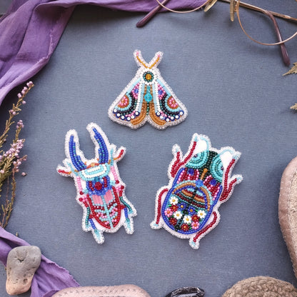 three colorful, intricately designed beaded objects arranged on a gray background.