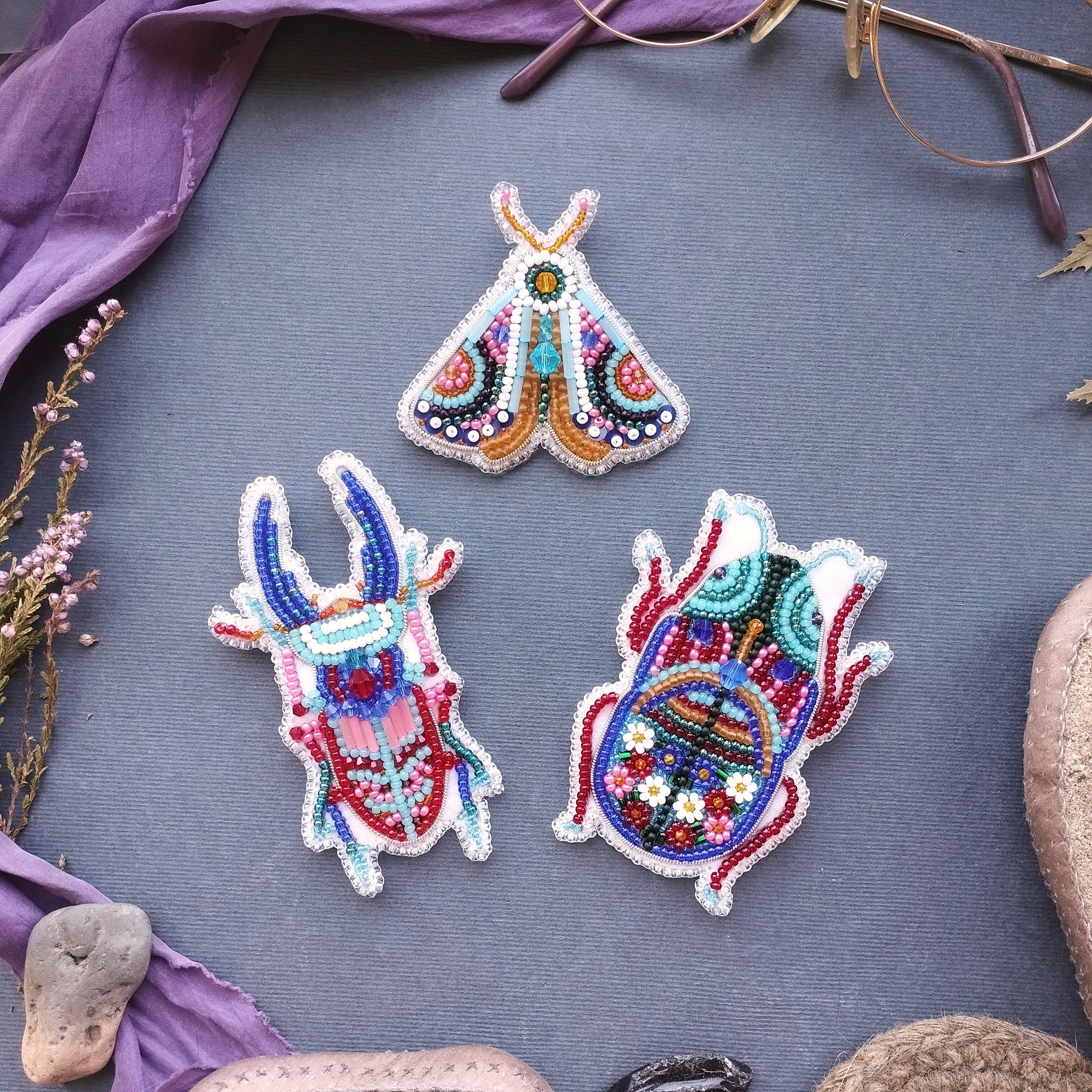 three colorful, intricately designed beaded objects arranged on a gray background.