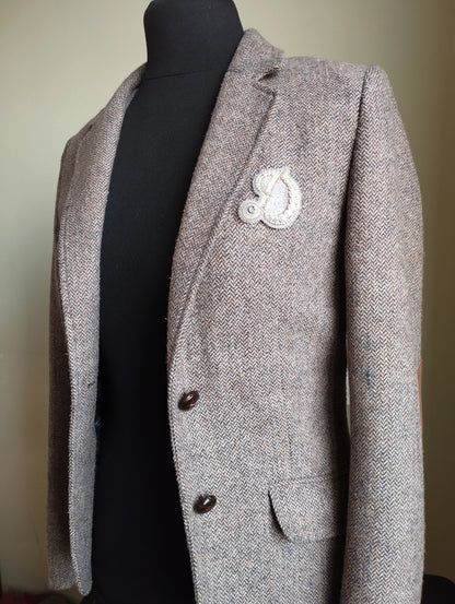 A gray tweed jacket with a white embroidered patch on the left chest area, displayed on a mannequin.