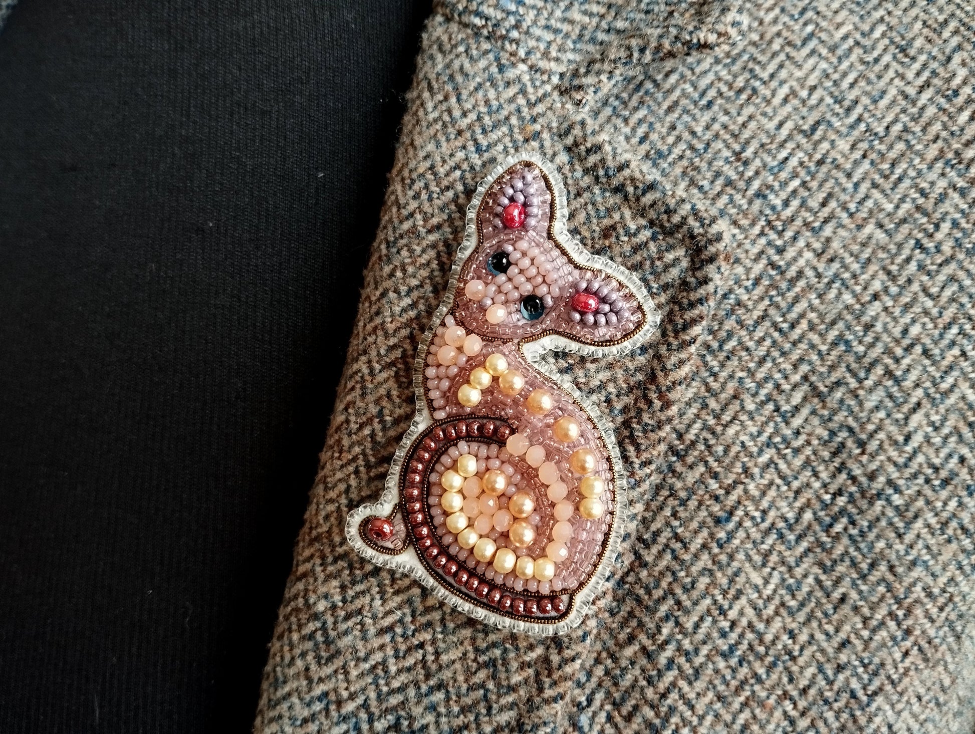 a close-up view of a cat-shaped embroidered patch on a fabric, with a dark background.