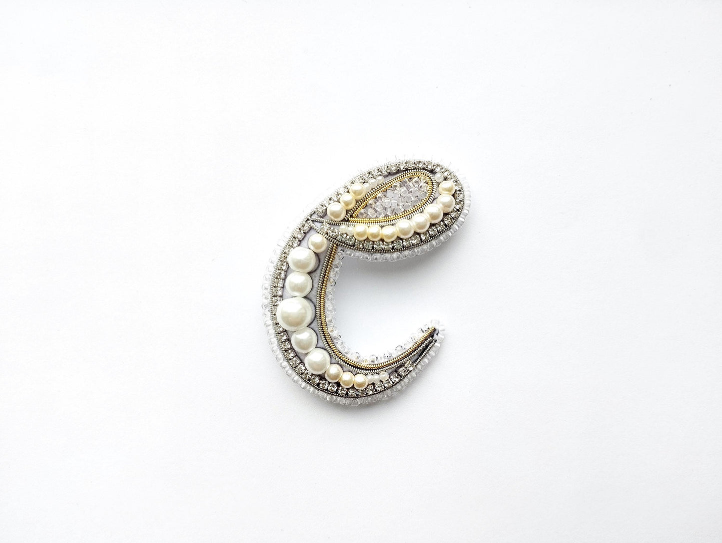 A decorative letter 'C' made of various materials, including pearls, beads, and crystals, against a white background.