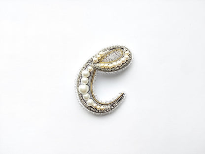 A decorative letter 'C' made of various materials, including pearls, beads, and crystals, against a white background.