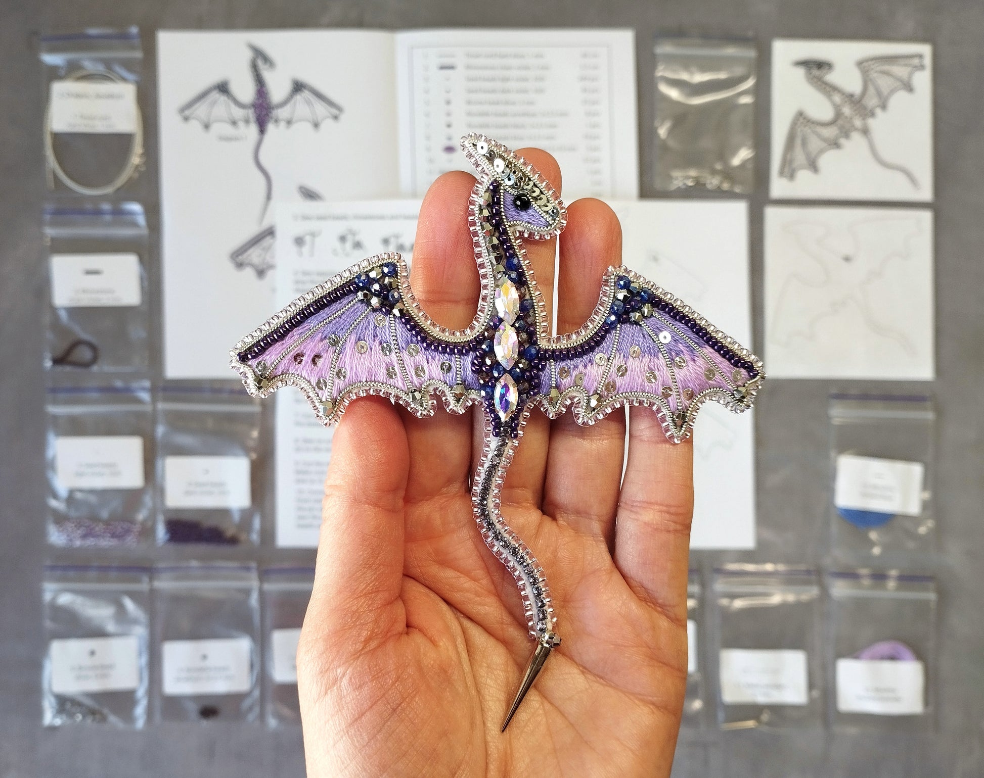 A hand holding a decorative dragon-shaped piece of jewelry, which appears to be made of beads and wire.