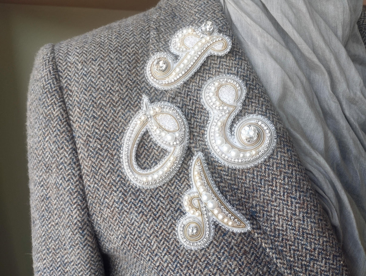 a close-up view of a person's shoulder, featuring a gray tweed jacket with decorative buttons and a scarf draped over the shoulder.