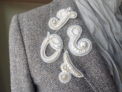 a close-up view of a person's shoulder, featuring a gray tweed jacket with decorative buttons and a scarf draped over the shoulder.