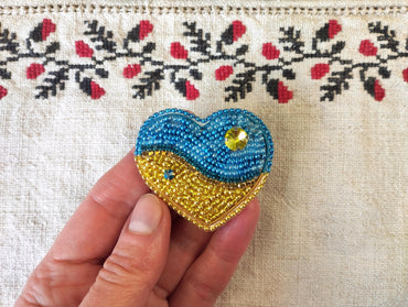 a hand holding a beaded heart on a piece of cloth