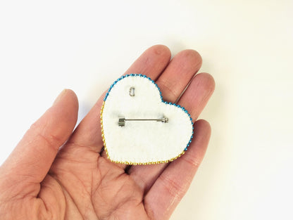 a hand holding a heart shaped brooch with an arrow on it