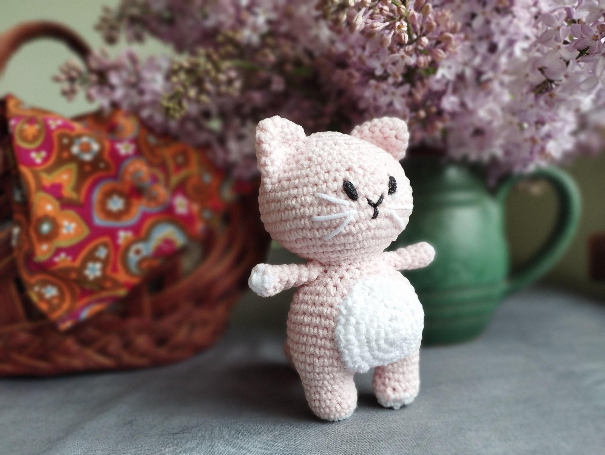 a crocheted cat sitting next to a basket of flowers