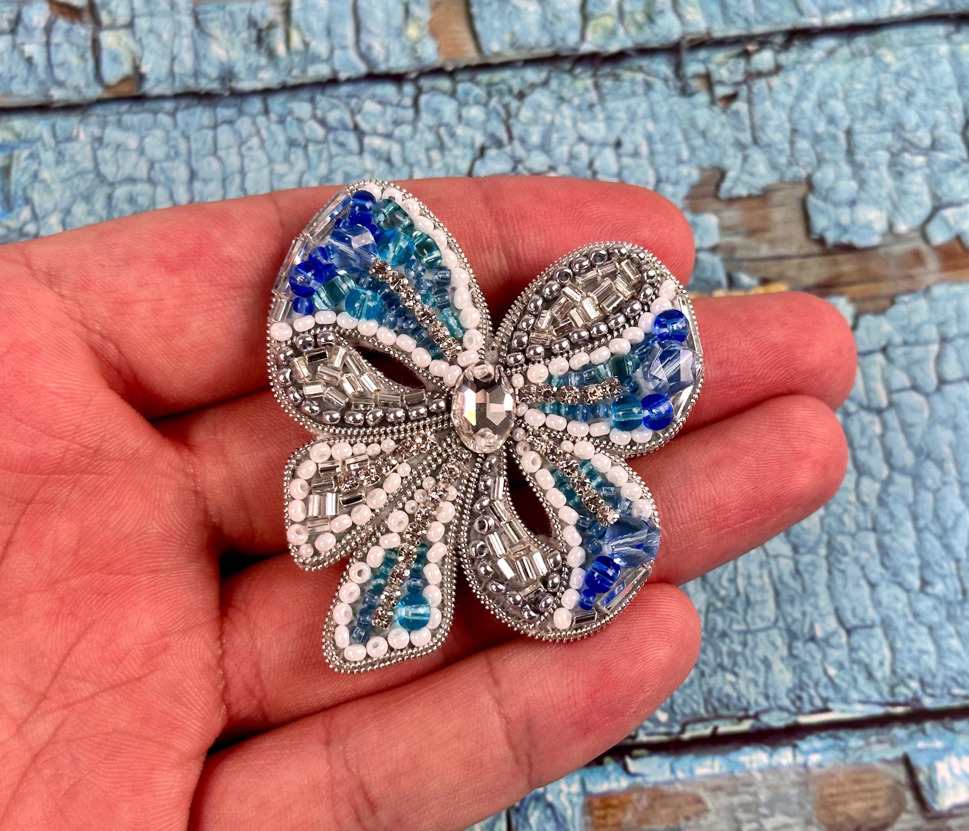 a hand holding a blue and white flower brooch