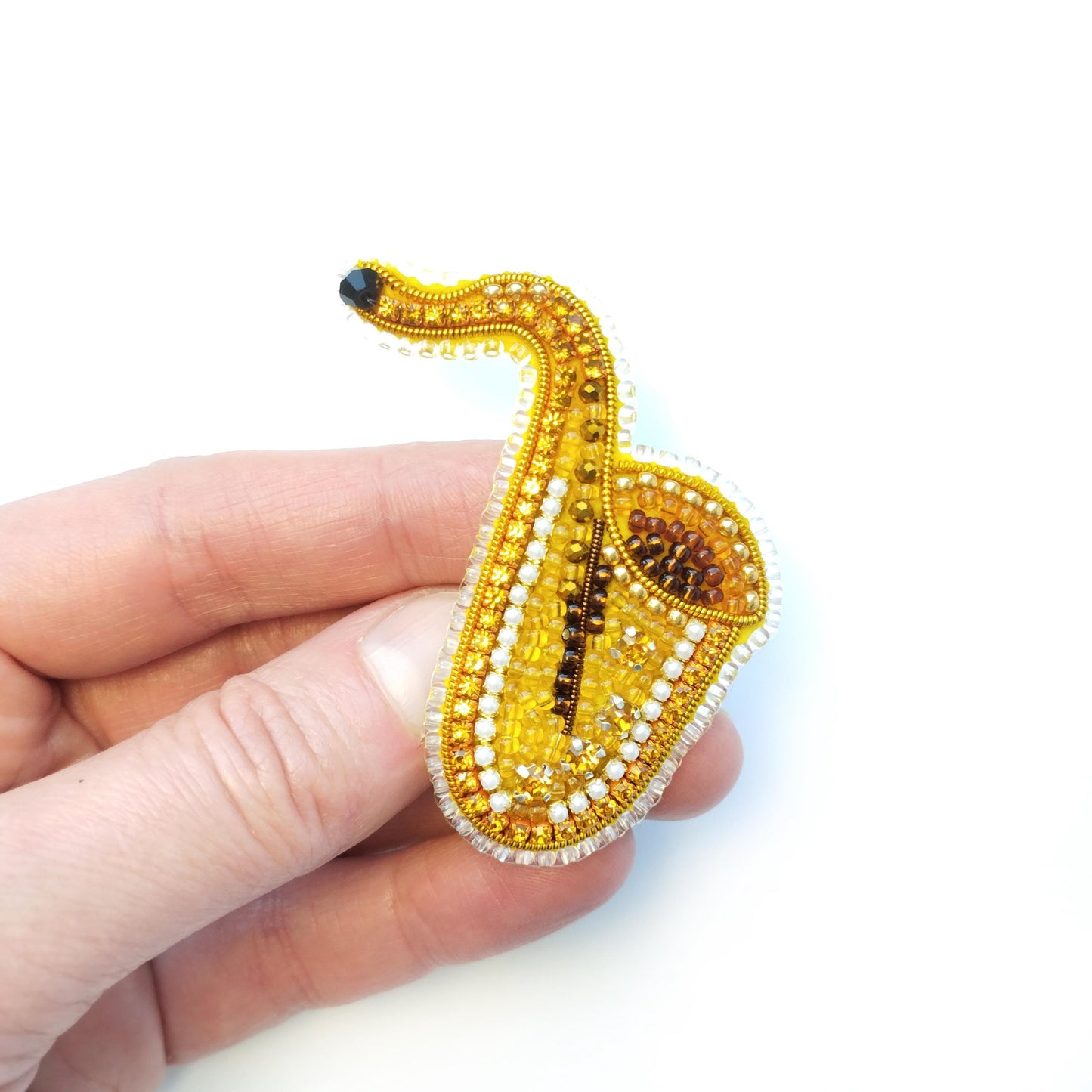 A hand holding a small, intricately designed beaded object resembling a saxophone.