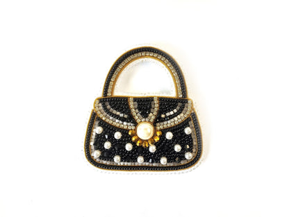 A handbag made of black beads and white pearls, with a gold-colored clasp and a large pearl at the center.