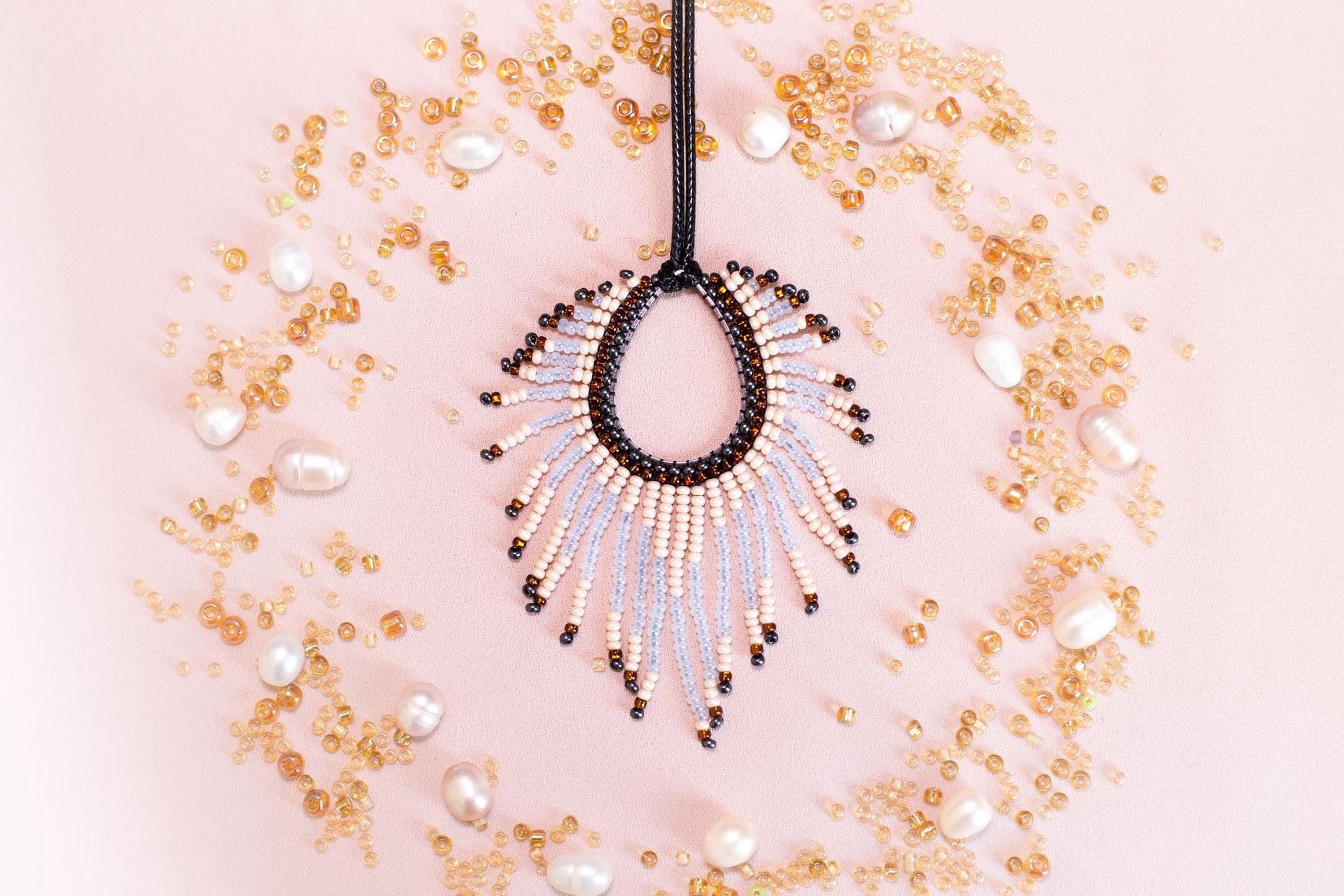 a beaded necklace with a large, open pendant surrounded by scattered pearls and beads in various shades of gold and white.