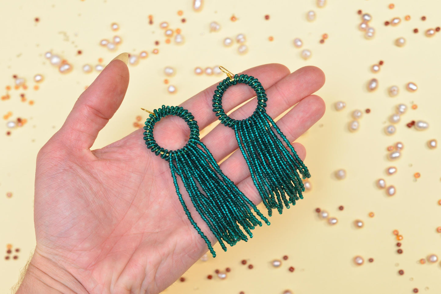a hand holding a pair of green beaded earrings