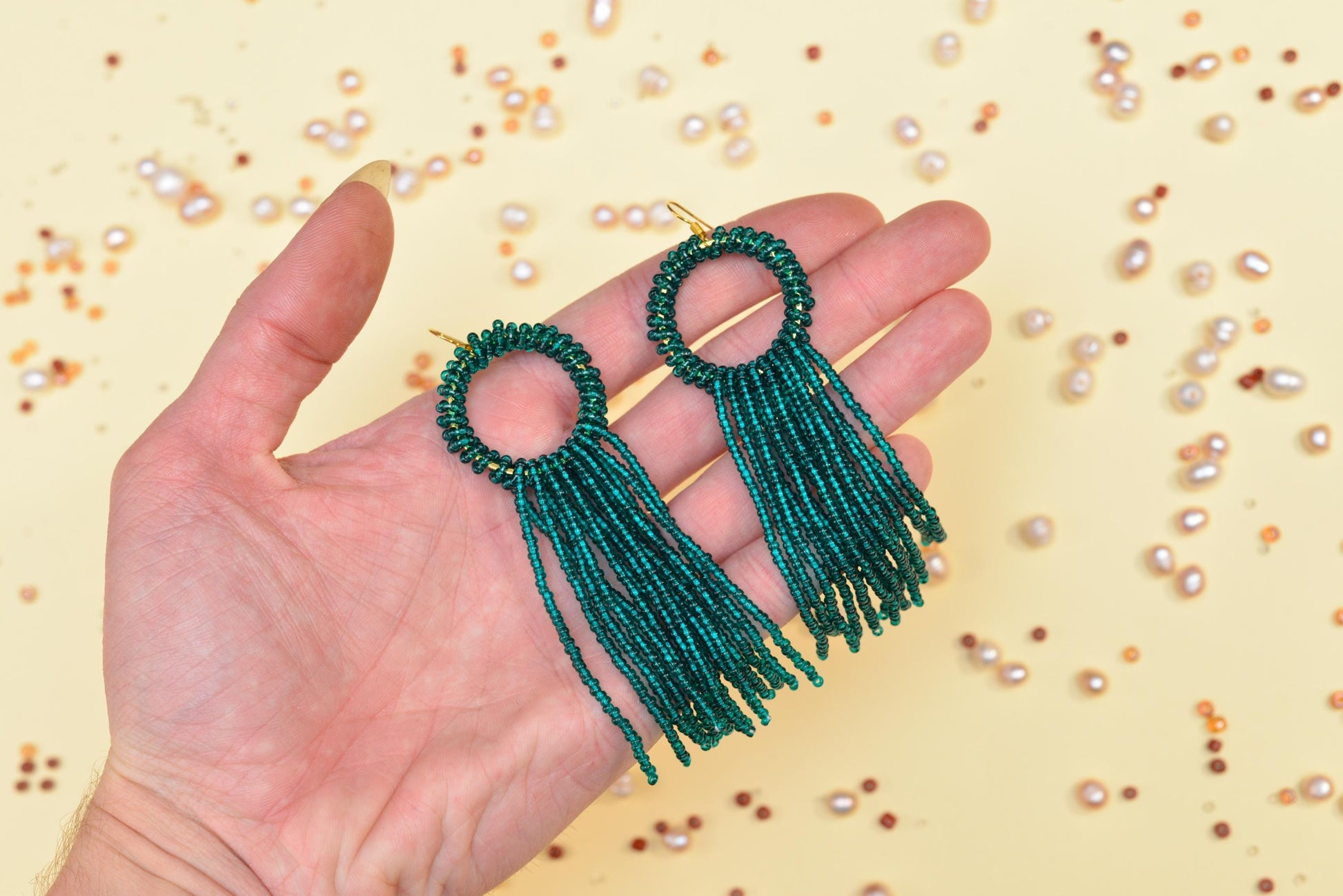 a hand holding a pair of green beaded earrings