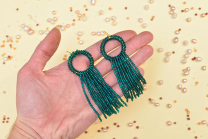 a hand holding a pair of green beaded earrings