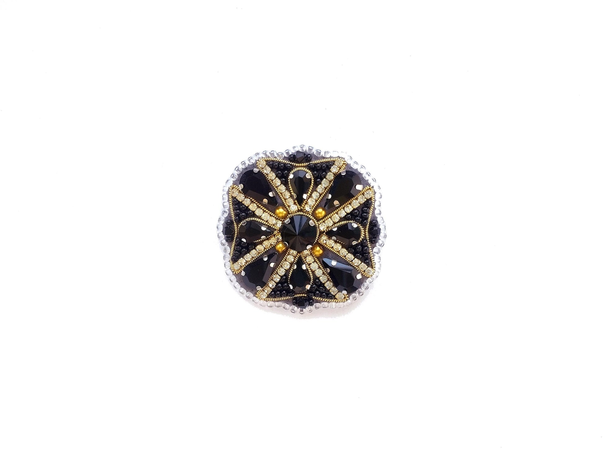 A decorative piece of jewelry with a black and gold design, featuring a central black gem surrounded by smaller black and gold stones arranged in a circular pattern.