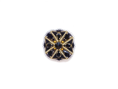 A decorative piece of jewelry with a black and gold design, featuring a central black gem surrounded by smaller black and gold stones arranged in a circular pattern.