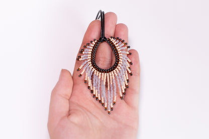 A hand holding a beaded earring with a fringe design.