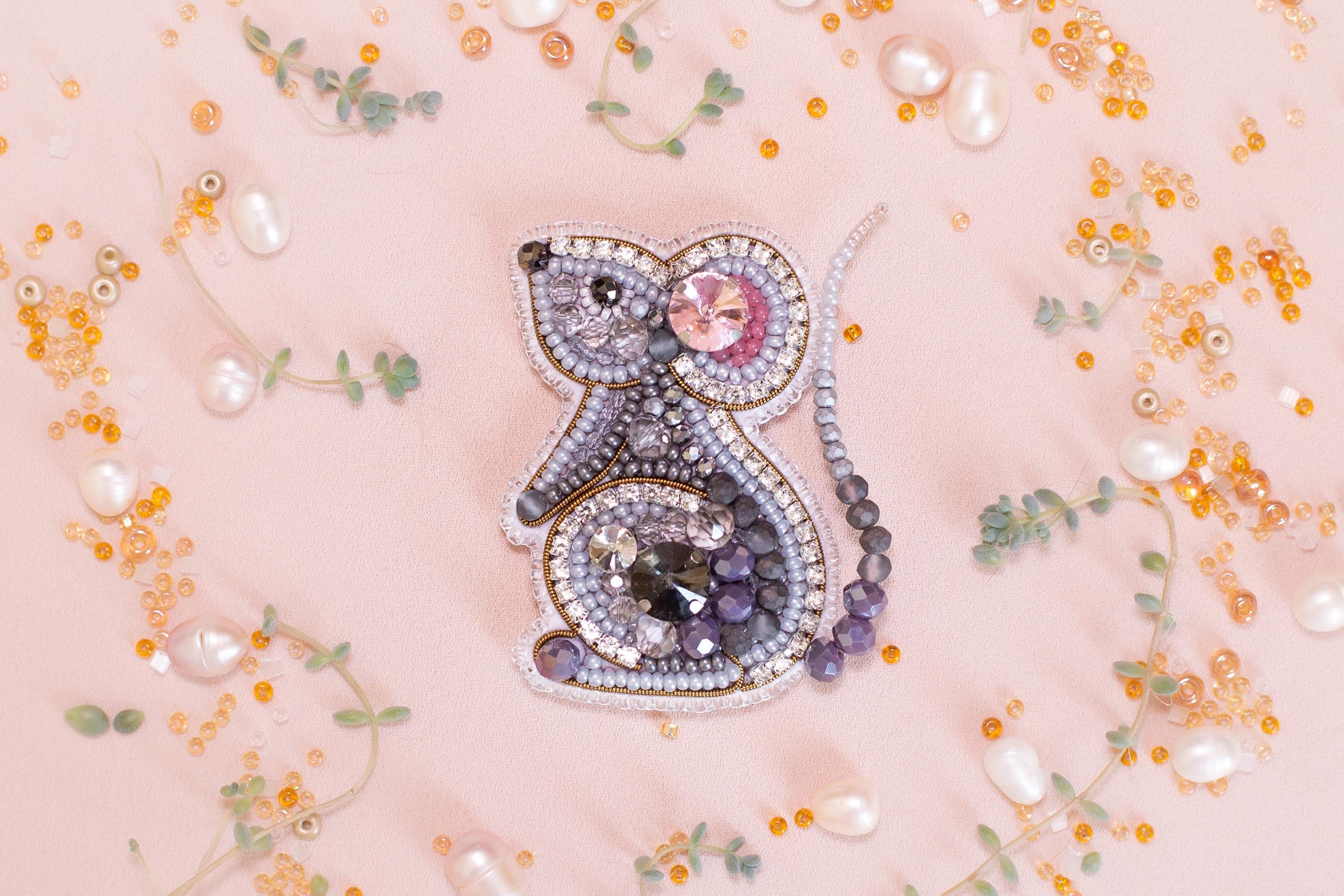 a decorative piece of jewelry, possibly a brooch or pendant, adorned with various gemstones and pearls. The jewelry piece is surrounded by an array of small, colorful beads and pearls, creating a visually appealing and intricate design.