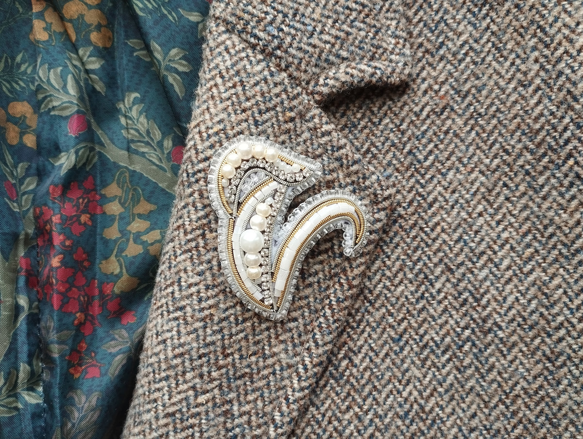 a close-up of a decorative brooch on a tweed jacket, with a floral patterned fabric visible in the background.