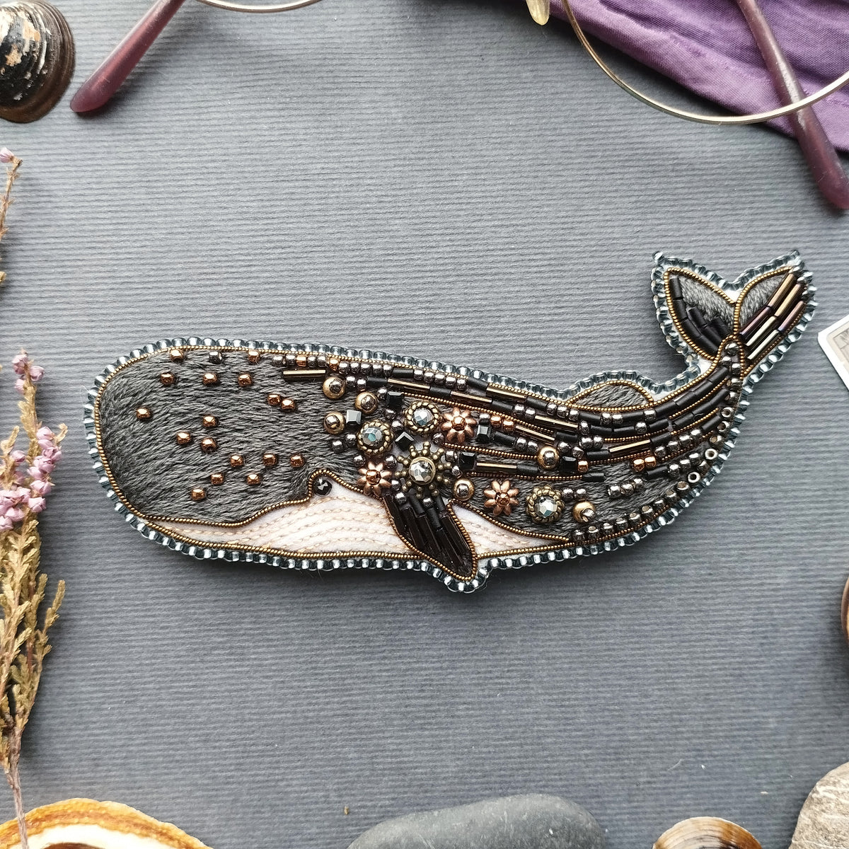 a detailed embroidered or beaded whale design, with intricate patterns and embellishments, placed on a gray surface.