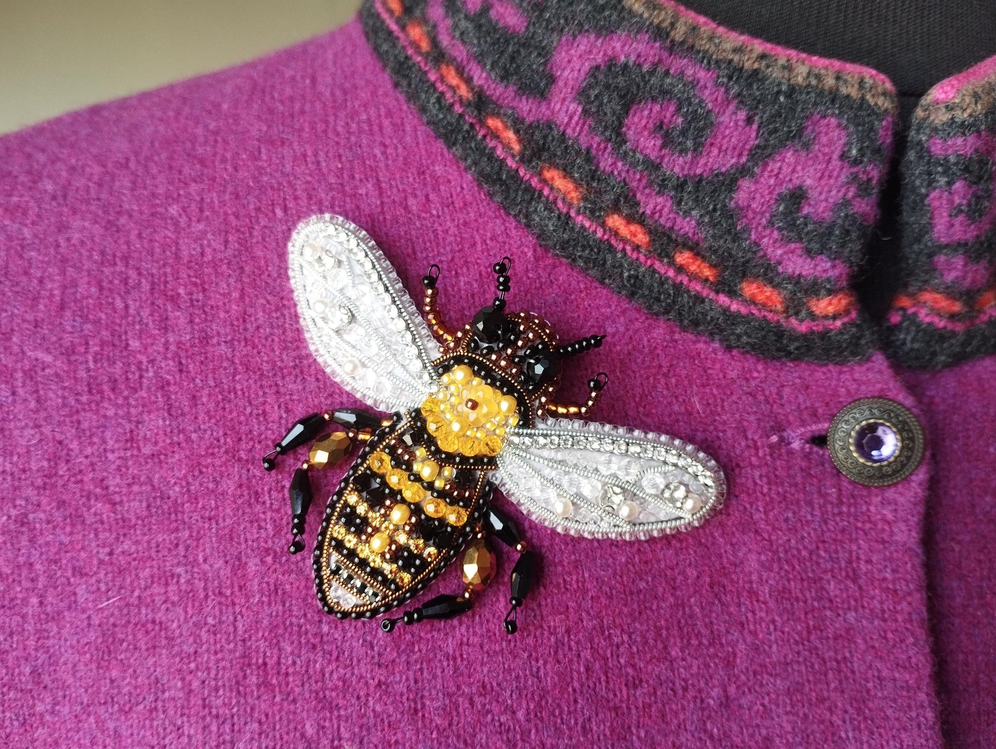 A close-up image of a purple sweater with a large, intricately designed bee embroidered on it.