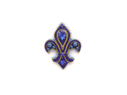 A decorative blue and gold brooch with a central gemstone surrounded by smaller gemstones and intricate designs.