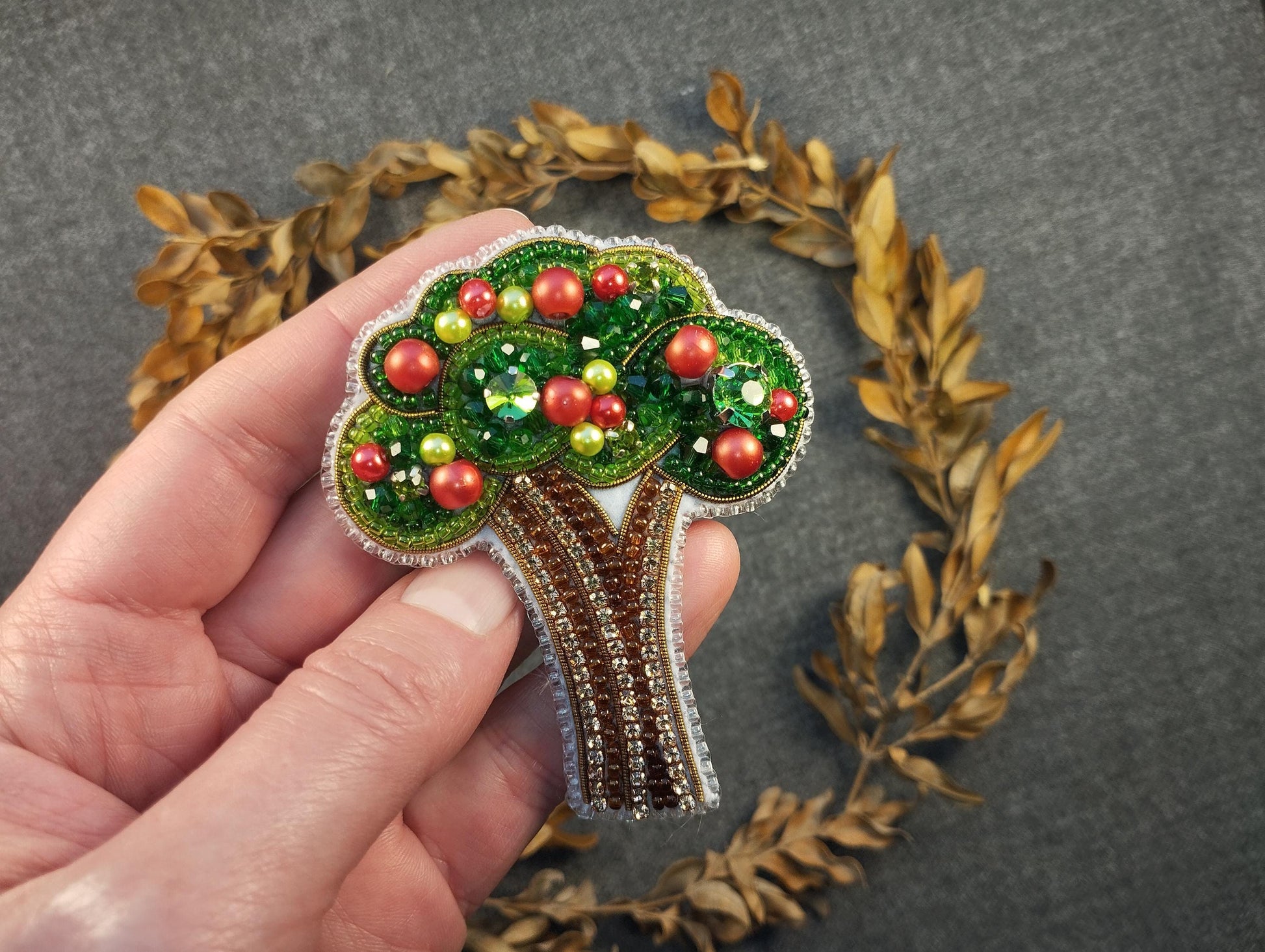 a hand holding a brooch with a tree on it