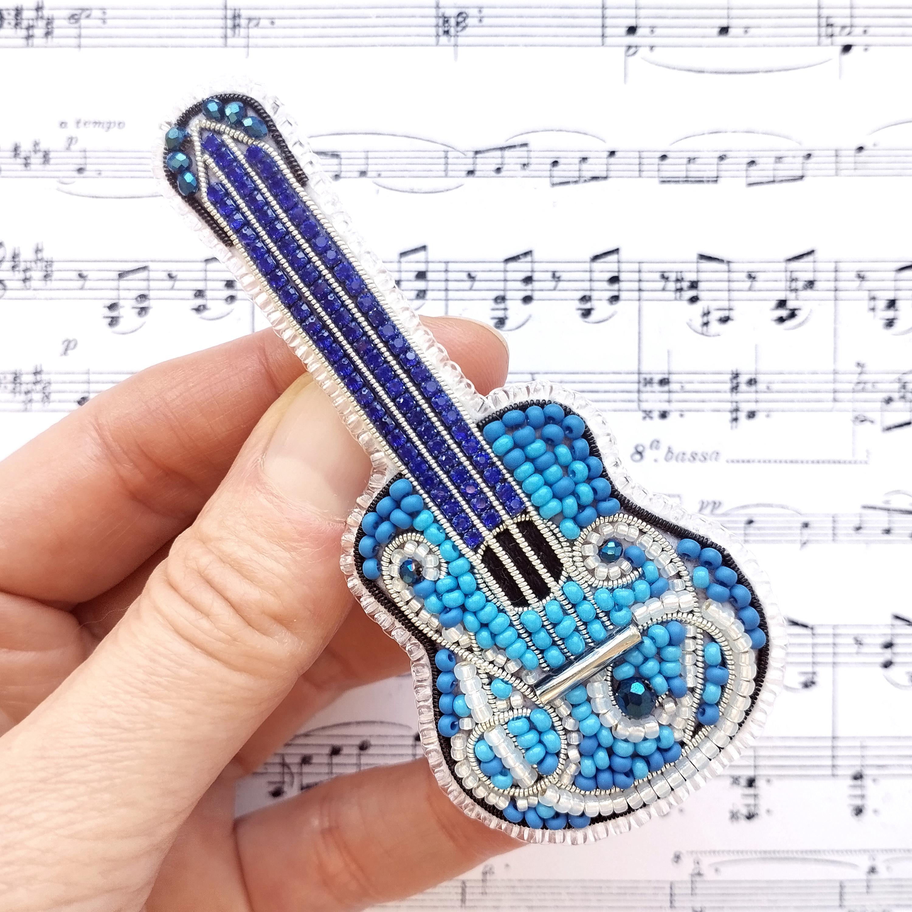 A hand is holding a small, intricately beaded guitar-shaped object against a background of sheet music.