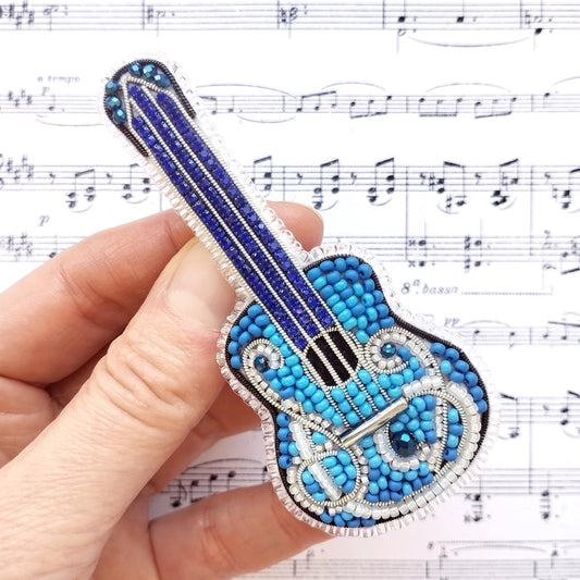 A hand is holding a small, intricately beaded guitar-shaped object against a background of sheet music.