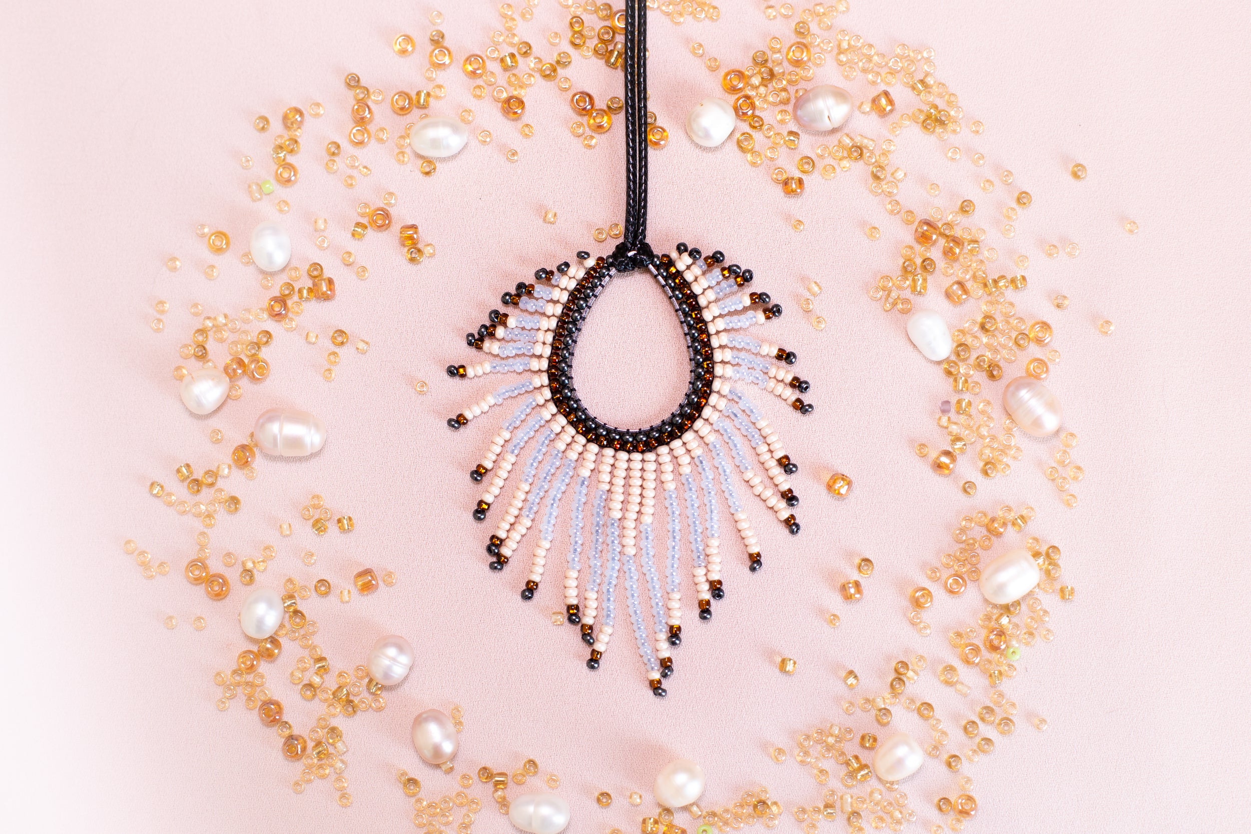 a beaded necklace with a large, open pendant surrounded by scattered pearls and beads in various shades of gold and white.