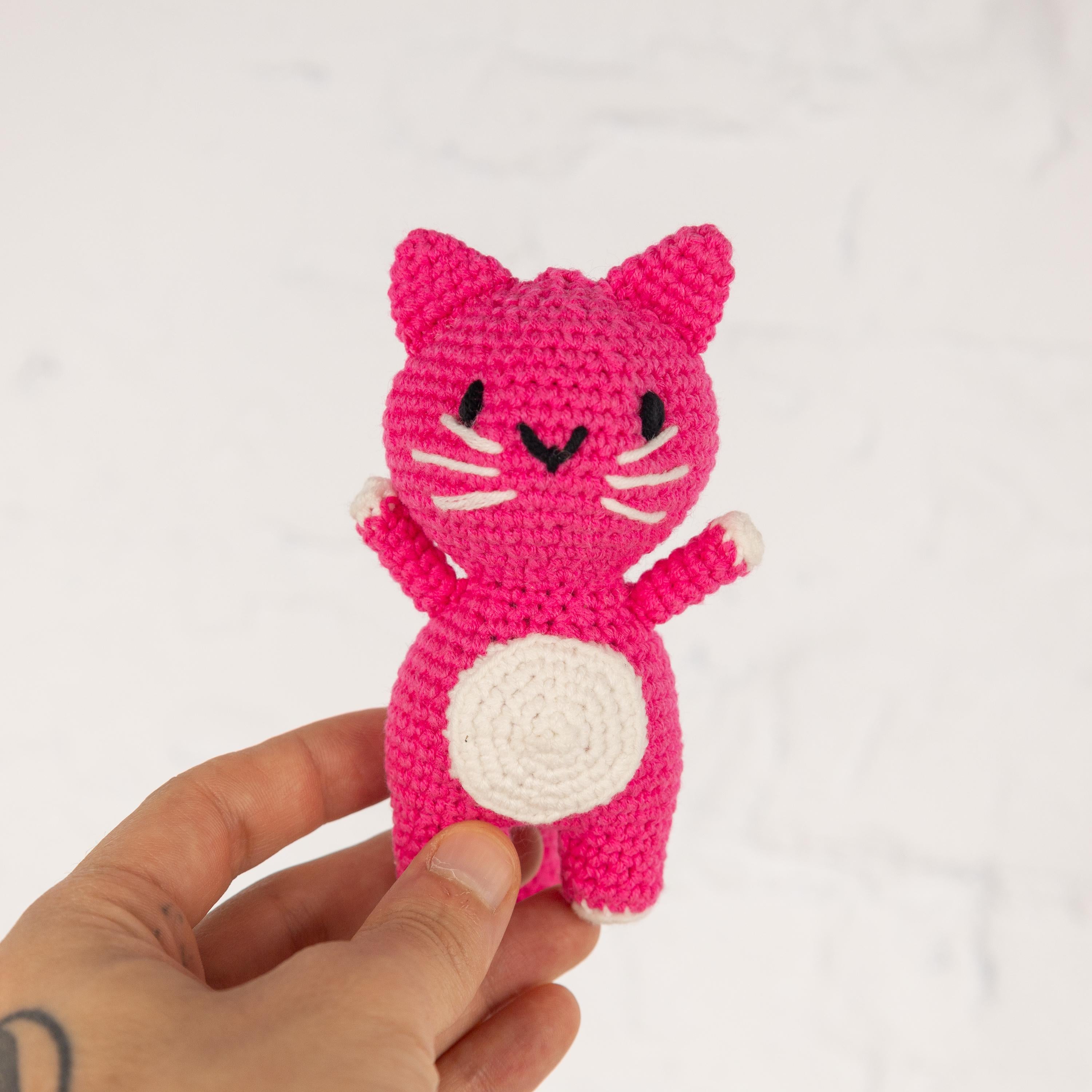 a hand holding a small pink crocheted cat