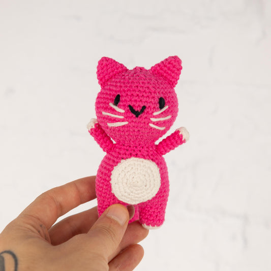 a hand holding a small pink crocheted cat