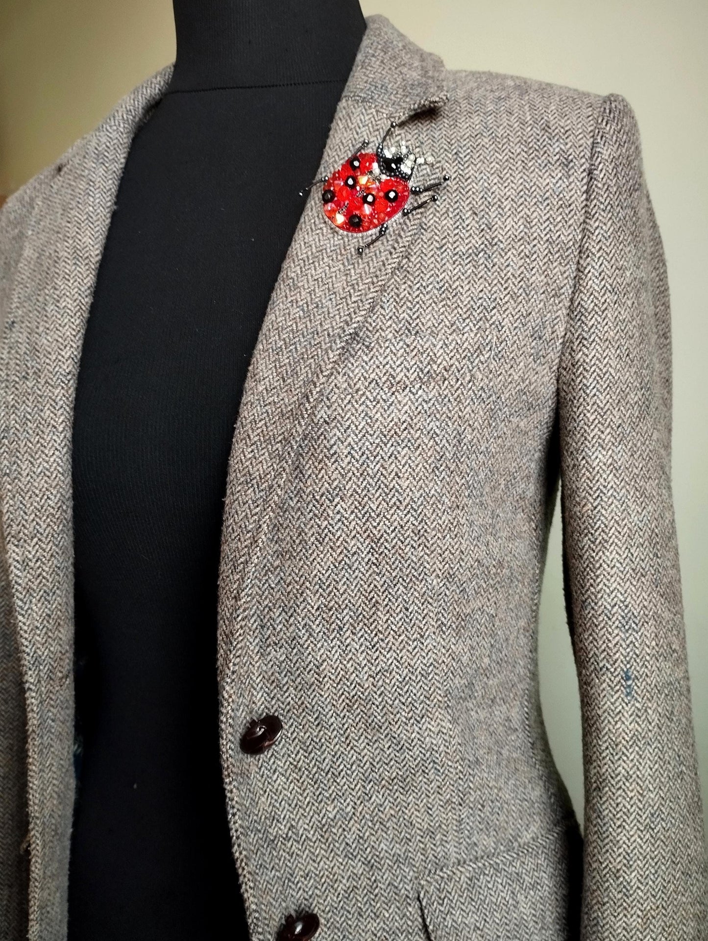 A gray tweed jacket with a red and black brooch featuring a ladybug design on the left chest area.