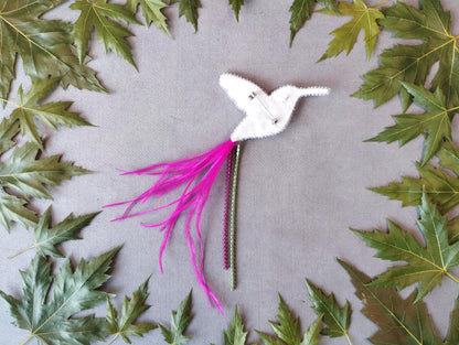 A white bird-shaped object with pink feathers and a green stem is surrounded by green leaves on a gray background.