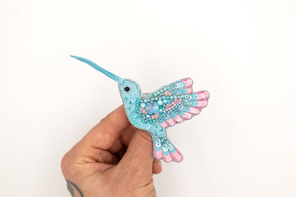 a hand holding a small blue and pink bird