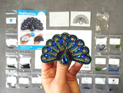 A hand holding a decorative peacock feather-shaped object, with various craft supplies and materials visible in the background.