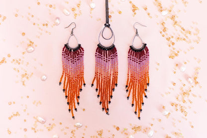 three beaded earrings with long, orange and purple fringe hanging against a pink background.