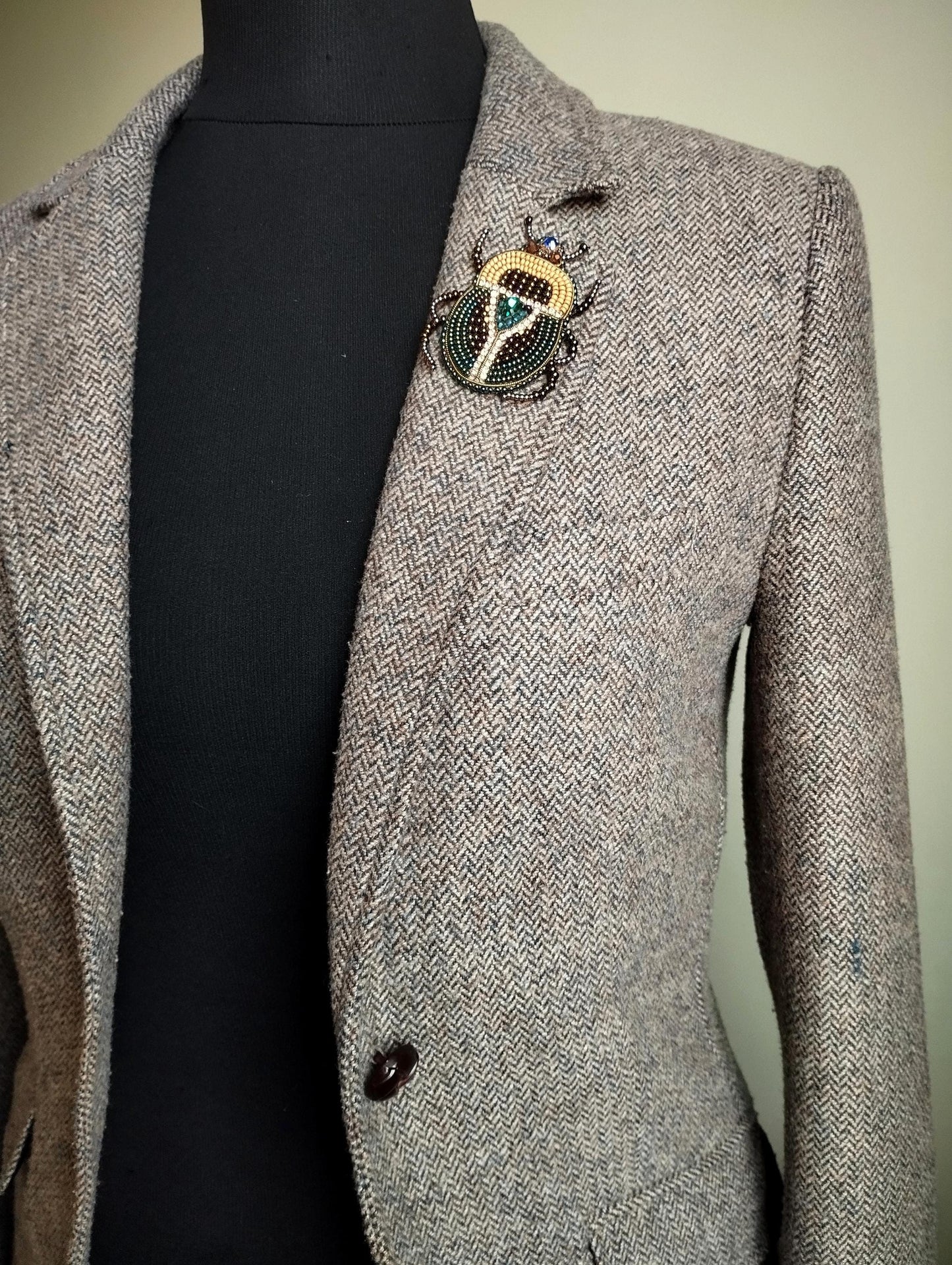 A gray tweed blazer with a decorative brooch on the left breast pocket area.