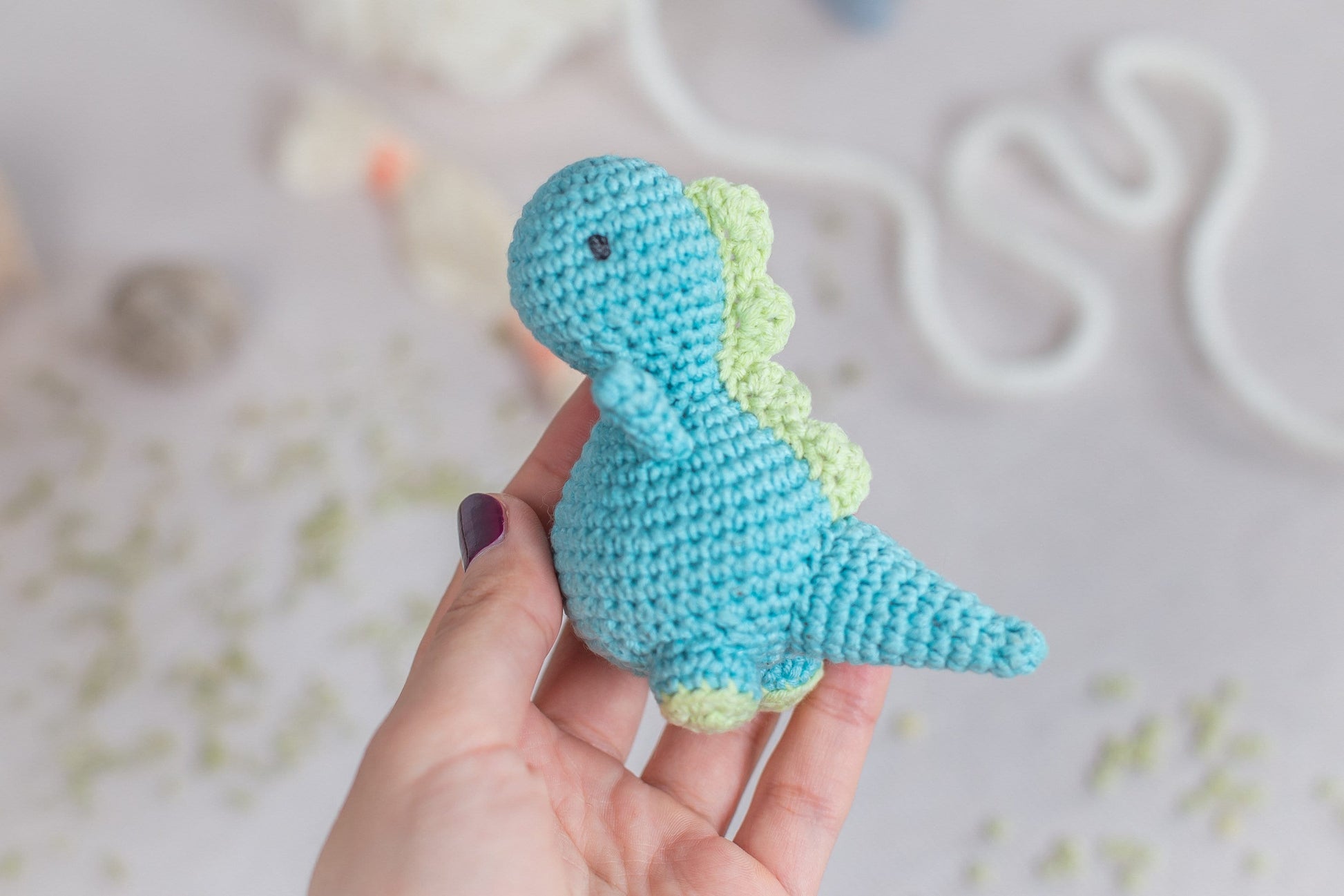 a hand holding a small crocheted toy dinosaur