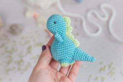 a hand holding a small crocheted toy dinosaur