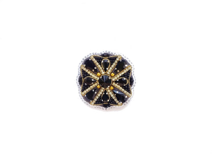A decorative piece of jewelry with a black and gold design, featuring a central black gem surrounded by smaller black and gold stones arranged in a circular pattern.