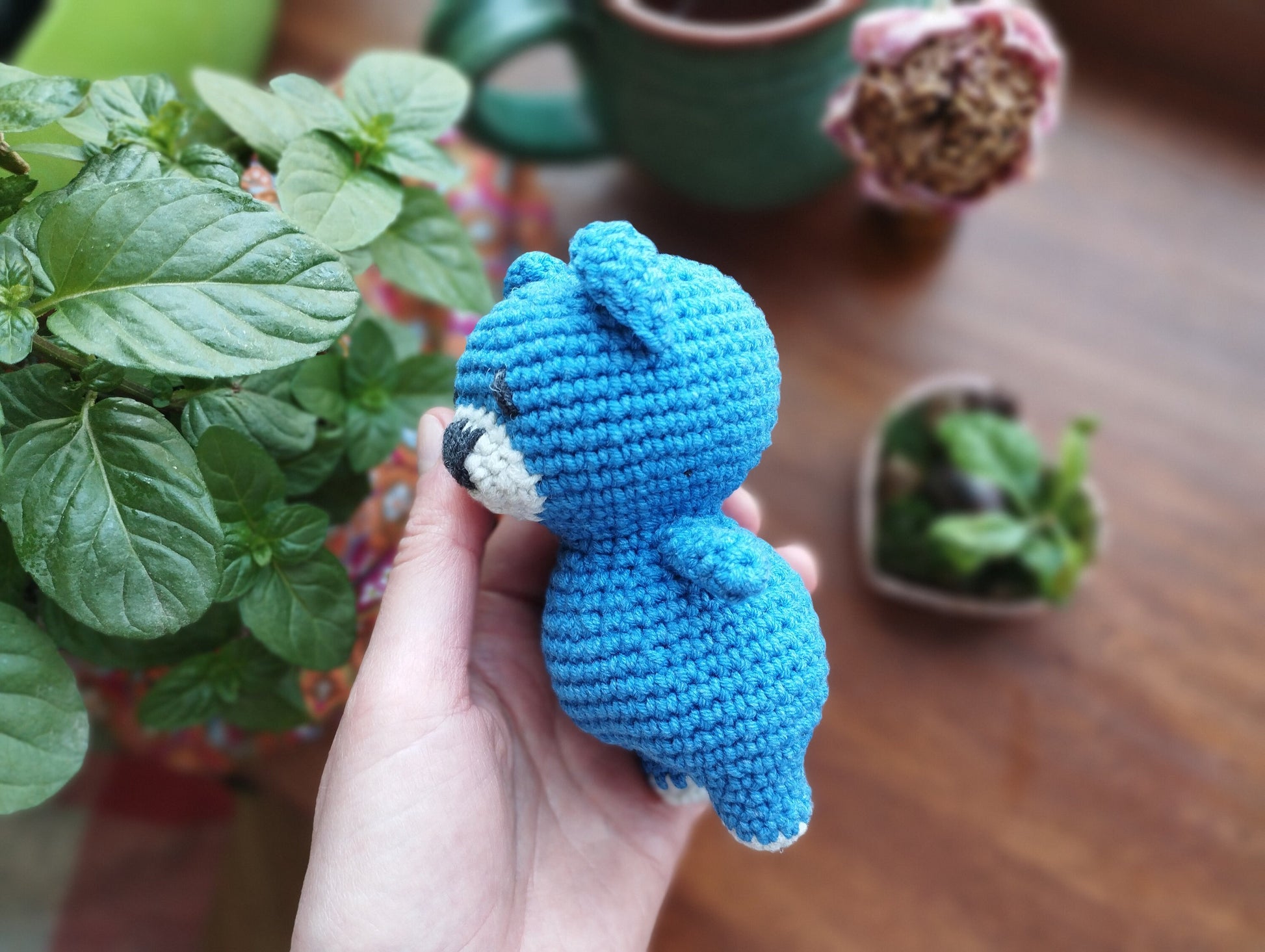 a hand holding a small crocheted blue teddy bear