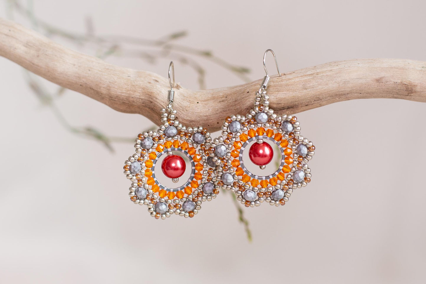 a pair of orange and silver earrings hanging from a branch