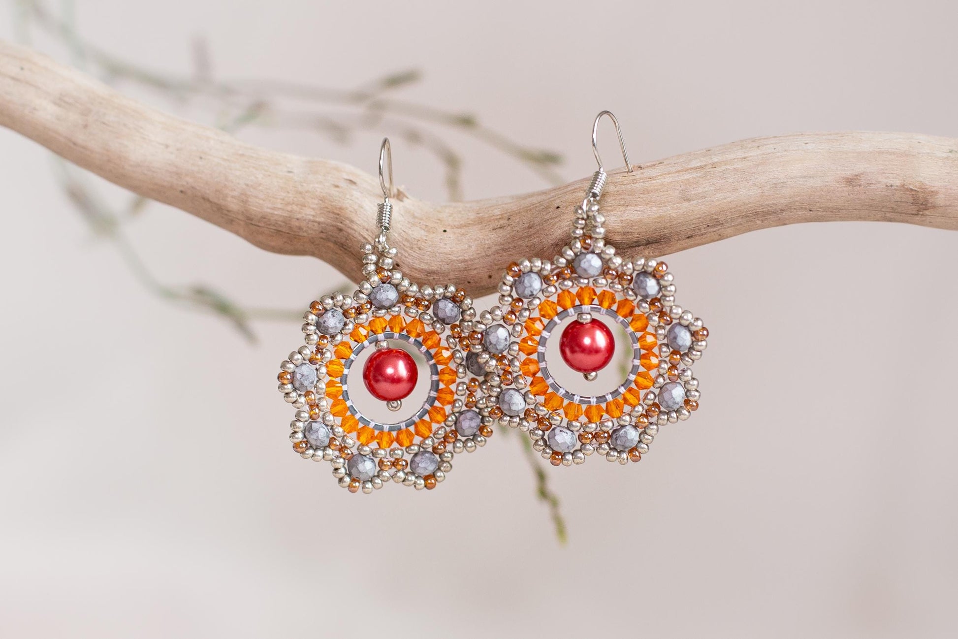 a pair of orange and silver earrings hanging from a branch